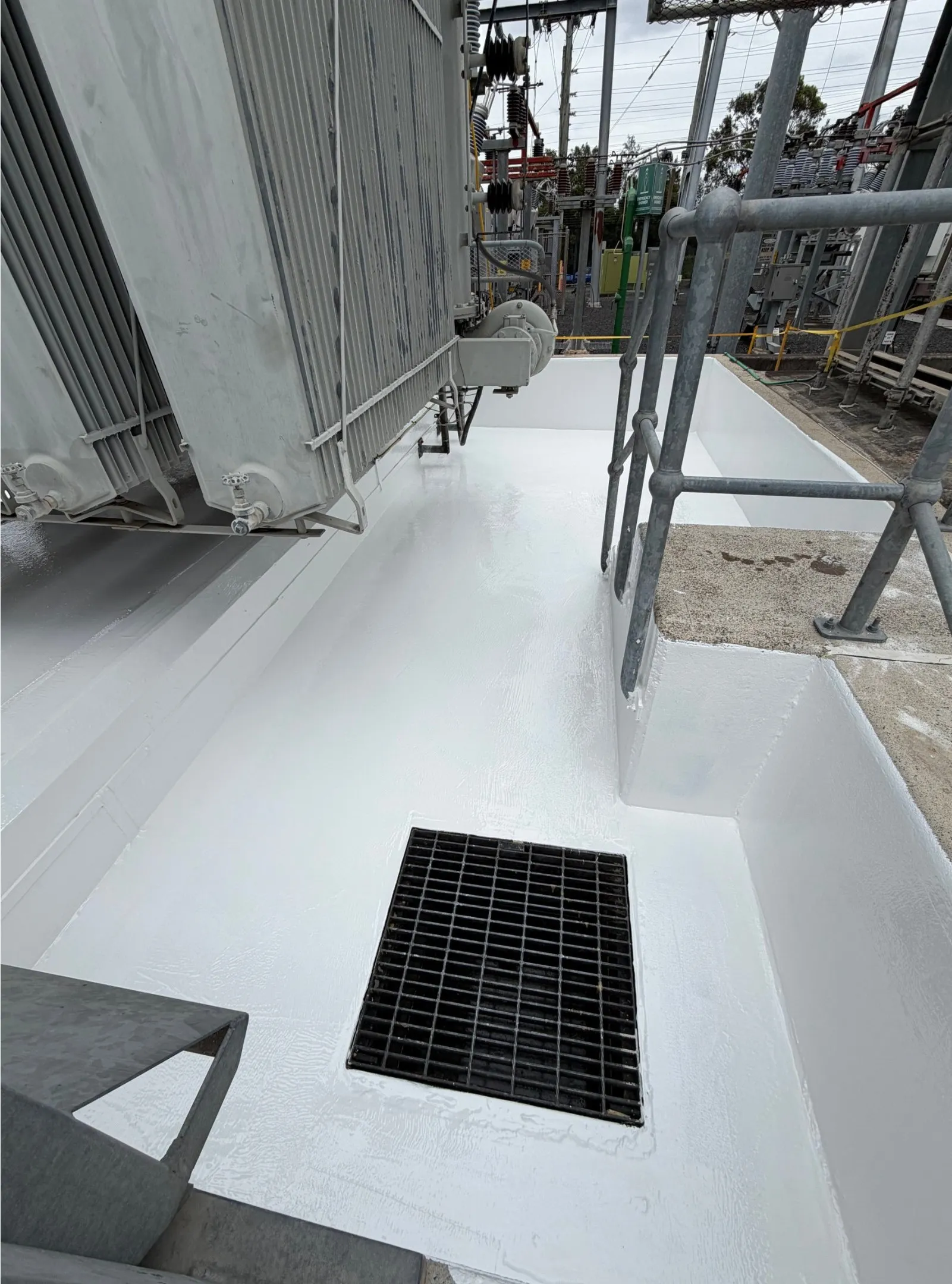 Completed white lining on a transformer bund floor, detailed around a drain grate and handrail posts.