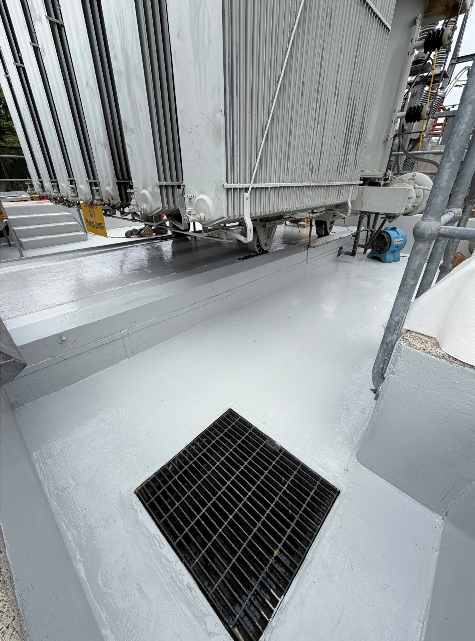 Grey first coat of a novolac lining applied to a transformer bund floor around a drain grate.